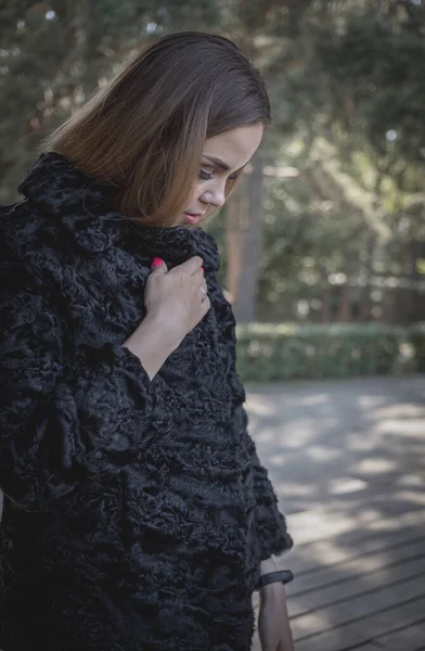 Uzun saçlı ve anlamlı gözlü güzel bir kız parkta kürk giymiş poz veriyor.