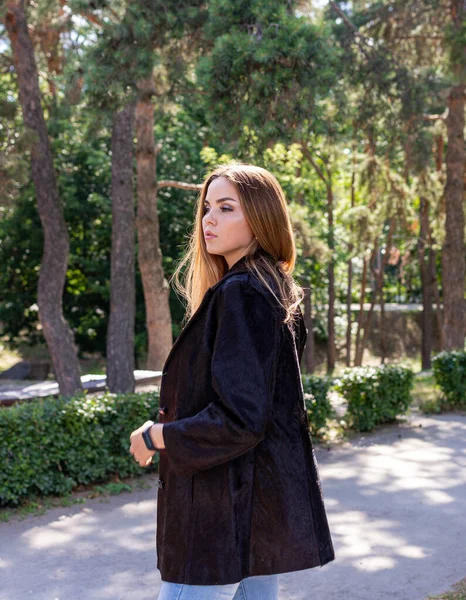 Uzun saçlı ve anlamlı gözlü güzel bir kız parkta kürk giymiş poz veriyor.
