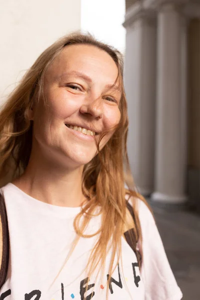 Beyaz tişörtlü ve kot pantolonlu güzel bir kız şehrin sokaklarında poz veriyor. Uzun saçları var ve makyajı yok. Eski şehrin mimarisi onun etrafında bir zemin.