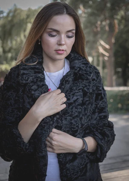 Uzun saçlı ve anlamlı gözlü güzel bir kız parkta kürk giymiş poz veriyor.