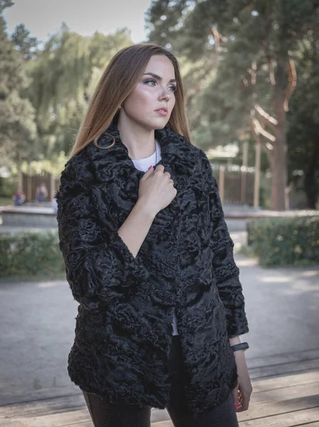 Uzun saçlı ve anlamlı gözlü güzel bir kız parkta kürk giymiş poz veriyor.