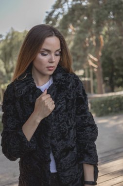 Uzun saçlı ve anlamlı gözlü güzel bir kız parkta kürk giymiş poz veriyor.