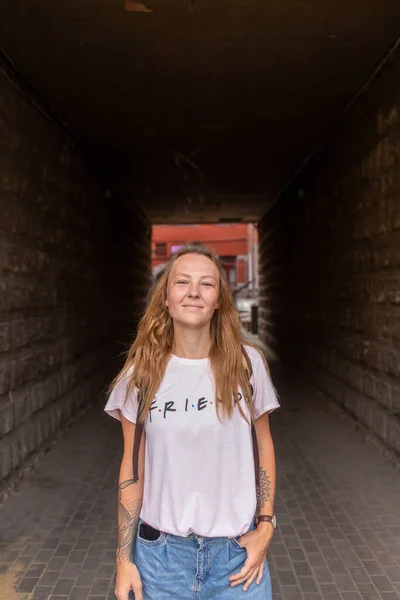 Beyaz tişörtlü ve kot pantolonlu güzel bir kız şehrin sokaklarında poz veriyor. Uzun saçları var ve makyajı yok. Eski şehrin mimarisi onun etrafında bir zemin.