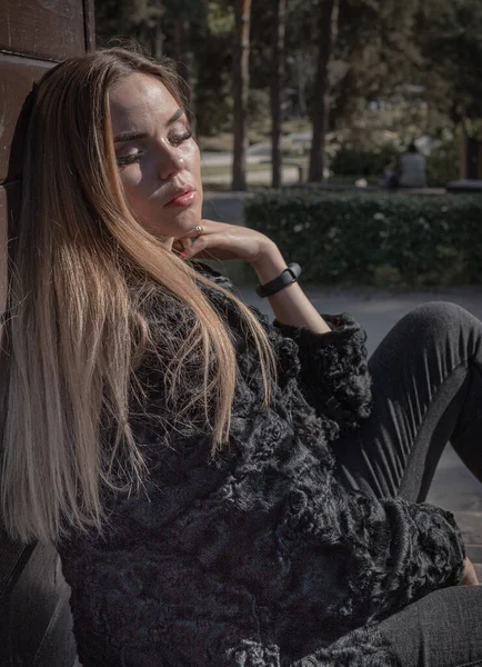 Ein schönes Mädchen mit langen Haaren und ausdrucksstarken Augen posiert in einem Pelzmantel in einem Park lizenzfreie Stockbilder