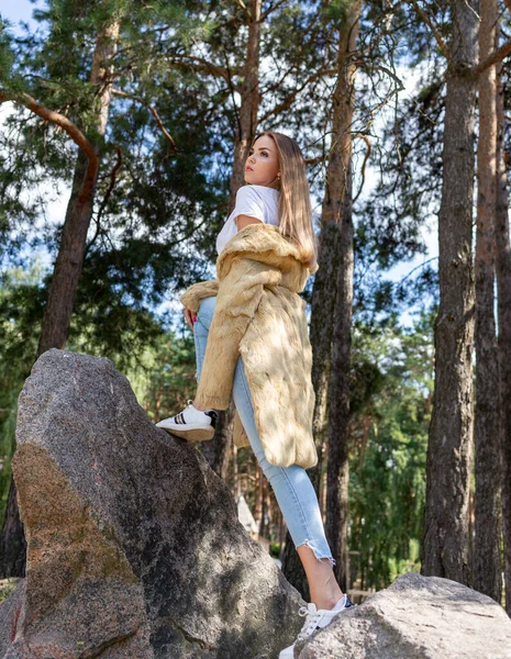 Uma menina bonita com cabelos longos e olhos expressivos posa em um casaco de pele em um parque — Fotografia de Stock