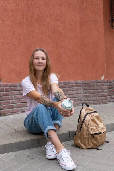 Beyaz tişörtlü ve kot pantolonlu güzel bir kız şehrin sokaklarında poz veriyor. Uzun saçları var ve makyajı yok. Eski şehrin mimarisi onun etrafında bir zemin.