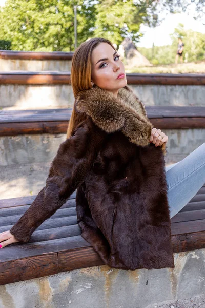 Uma menina bonita com cabelos longos e olhos expressivos posa em um casaco de pele em um parque — Fotografia de Stock