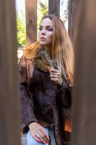 Een mooi meisje met lang haar en expressieve ogen poseert in een bontjas in een park — Stockfoto