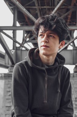 Doğu görünümlü, siyah saçlı, yakışıklı ve etkileyici yüzlü genç bir adam ağaçların ve mimarinin arka planına karşı parkta poz veriyor.