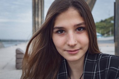 Çek ceketli ve bej pantolonlu güzel bir genç kız parkta kameraya poz veriyor. Uzun saçlı profesyonel bir model.