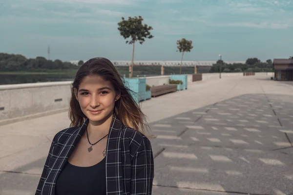 Uma menina bonita em uma jaqueta verificada e calças bege posa para a câmera em um parque. modelo profissional com cabelo comprido — Fotografia de Stock