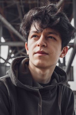 Doğu görünümlü, siyah saçlı, yakışıklı ve etkileyici yüzlü genç bir adam ağaçların ve mimarinin arka planına karşı parkta poz veriyor.