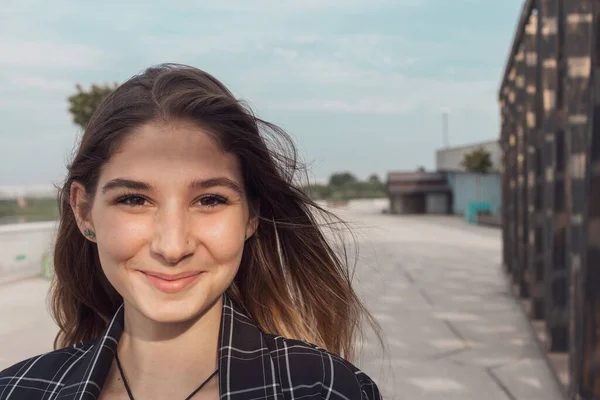 Uma menina bonita em uma jaqueta verificada e calças bege posa para a câmera em um parque. modelo profissional com cabelo comprido — Fotografia de Stock