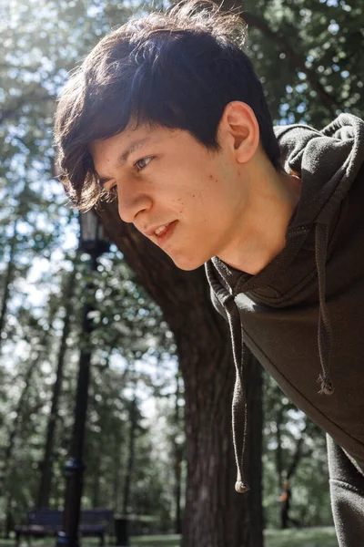 A young guy of Eastern appearance with black hair and a handsome expressive face poses in a Park against the background of trees and architecture — Stock Photo, Image