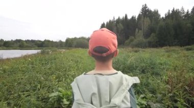 Genç maceraperest, beysbol şapkası takmış dingin bir gölün kenarındaki yeşil çayırlarda dolaşırken doğanın sükunetini ve güzelliğini tamamen kucaklıyor.