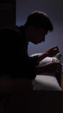 Dikey video silueti, geceleri yatağının kenarında oturan, uykusuzluk ve kaygı ile boğuşan, zihinsel sağlık ve duygusal refahla mücadeleyi vurgulayan bir genç adam.