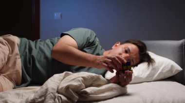 Genç adam geceleri yatakta yatarken renkli bir bulmacayla oynuyor. Uyumadan önce çözmeye çalışıyor. Rahatlatıcı bir aktiviteye girişiyor.