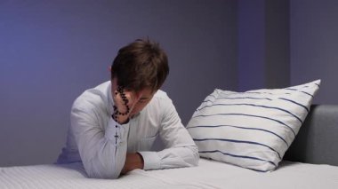 Tespih taşıyan ve geceleri yatakta dua eden bir adam, kutsal bir inanç ve yalnızlık anı umut, bağlılık, tefekkür ve sessiz ruhsal rahatlık iletir.