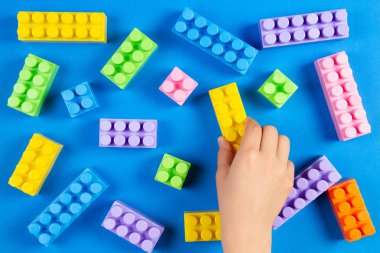 Çocuklar el mavi arka plan üzerinde renkli plastik inşaat bloklarla oynama