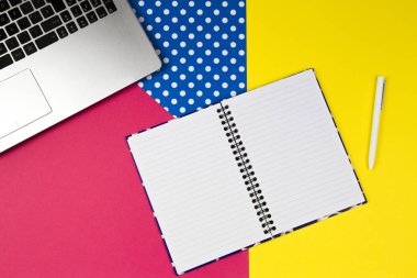 Renkli çalışma alanı. Dizüstü bilgisayar açık renkli arka plan üzerinde beyaz kalem ve kağıt defter