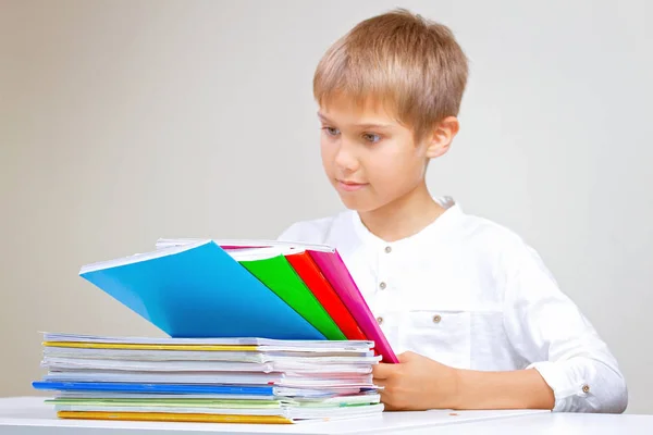 Kind zijn huiswerk thuis. De jongen zitten en kijken in boeken, notebooks en leerboeken — Stockfoto