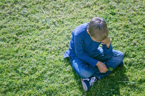 Unglücklicher trauriger aufgebrachter Junge, der allein auf dem Gras sitzt — Stockfoto