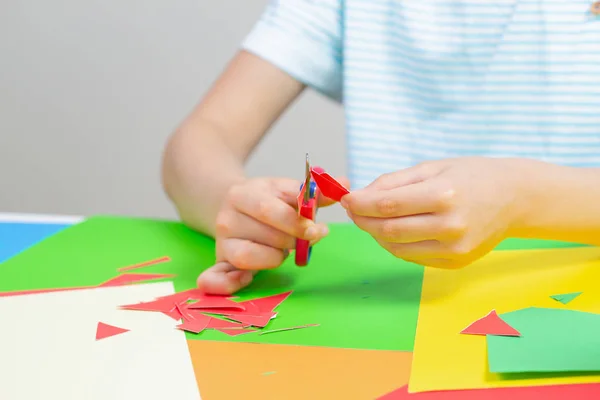 Kinderhände schneiden buntes Papier mit der Schere am Tisch — Stockfoto