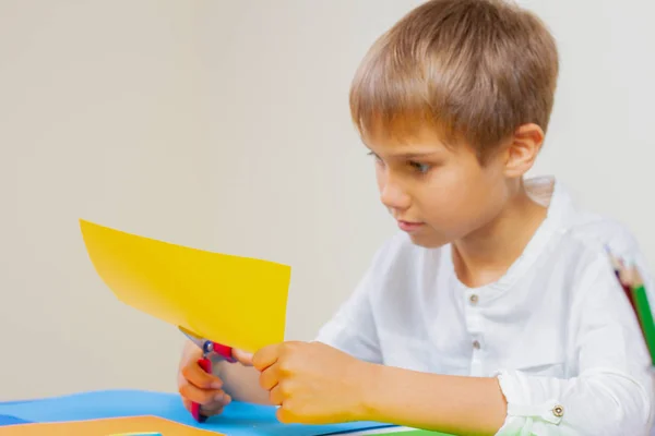 Criança cortando papel colorido com tesoura na mesa — Fotografia de Stock