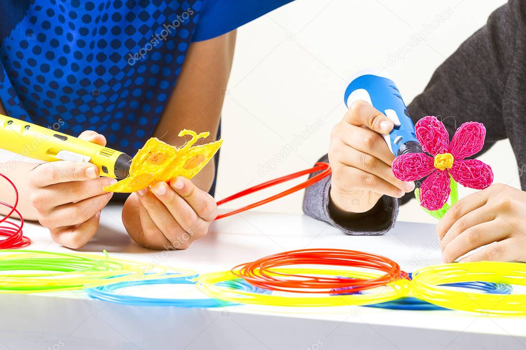 Kids hands with 3d pens and colorful filaments on white table