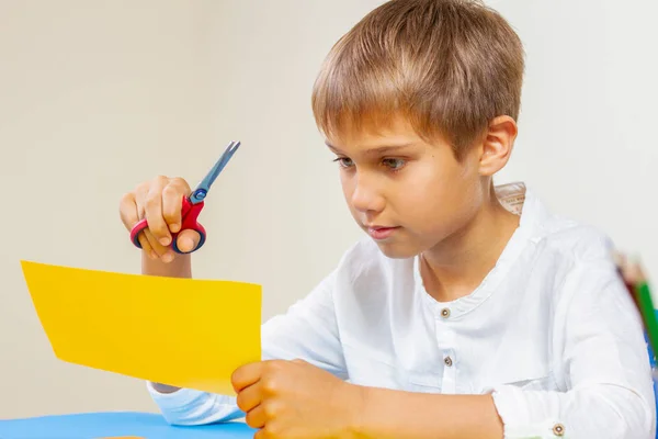 Bambino che taglia carta colorata con le forbici a tavola — Foto Stock