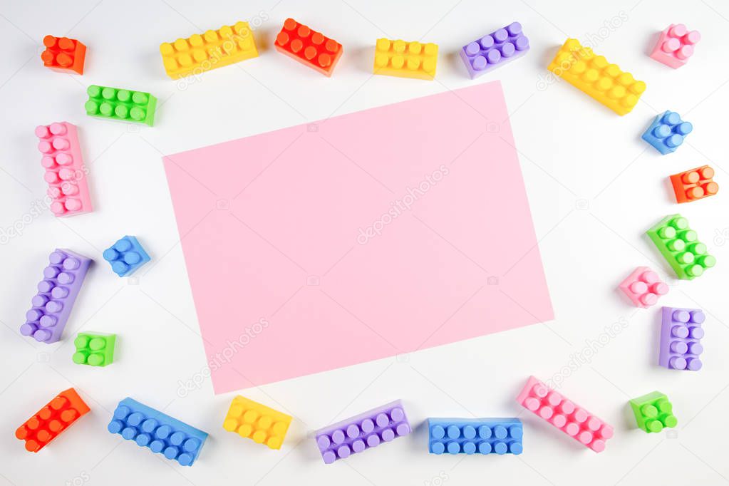Colorful plastic construction blocks frame with pink blank card on white background.