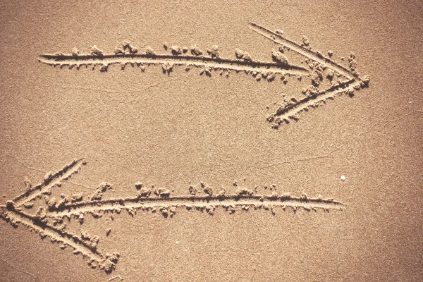 Dois sinais de seta desenho em fundo de areia — Fotografia de Stock