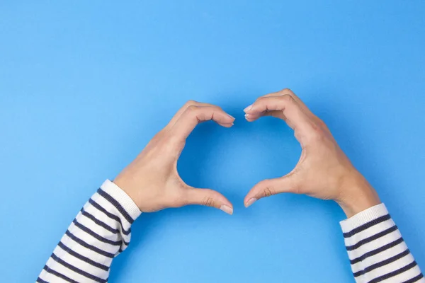 Eller kadın mavi arka plan üzerinde bir kalp şekil verme — Stok fotoğraf