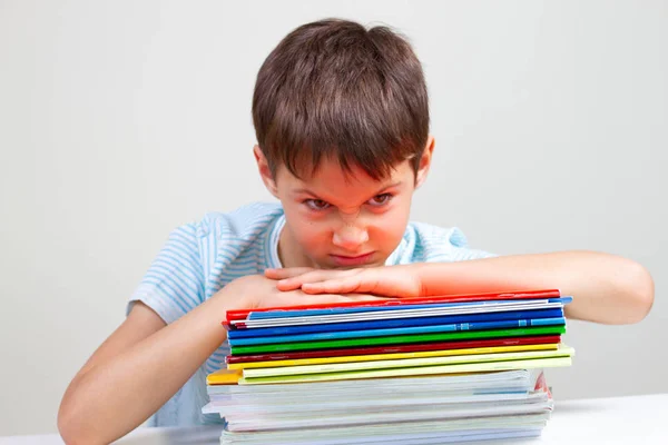 Estudante irritado sentado na mesa com pilha de livros escolares e cadernos — Fotografia de Stock