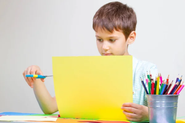 Jongen gekleurd papier knippen met een schaar aan de tafel — Stockfoto