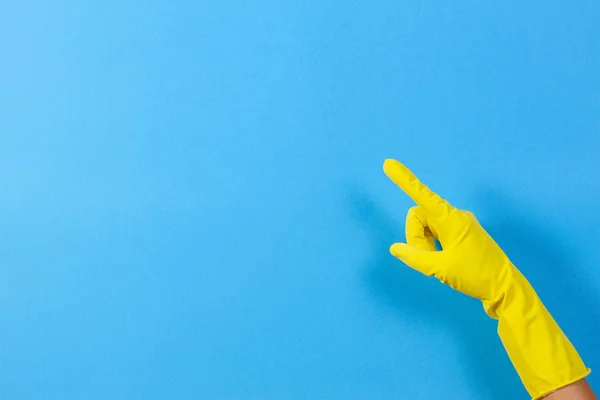 Ręka kobiety z żółty gumowe rękawice punktów do góry z palcem wskazującym, niebieskie tło — Zdjęcie stockowe