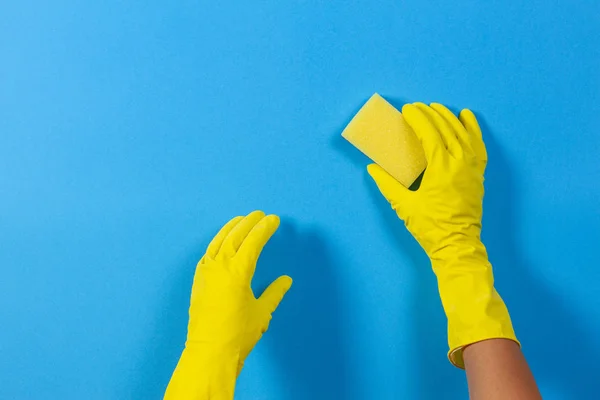 Mãos em luvas amarelas com esponja sobre fundo azul — Fotografia de Stock