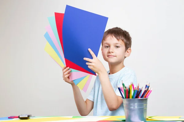 Мальчик с цветной бумагой сидит за столом — стоковое фото