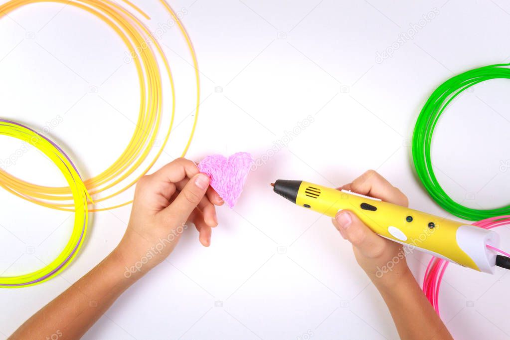 Kids hand holding yellow 3d pen with colorful filaments and makes heart on white background