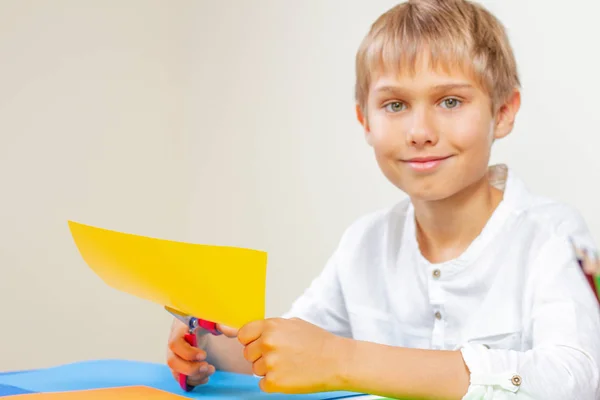 Bambino che taglia carta colorata con le forbici a tavola — Foto Stock