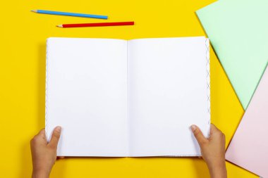 Çocuk elleri açık kitap defter ve sarı renkli arka planla