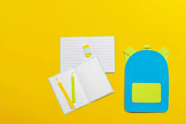 School bag backpack, notebooks and pencils paper cut on yellow background — Stock Photo, Image