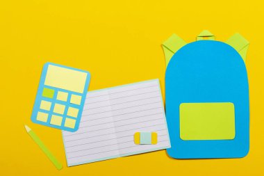 Okul eğitim Kağıt arka plan. Okul çantası sırt çantası, Notebook ve hesap makinesi kağıt üzerinde sarı arka plan kesmek
