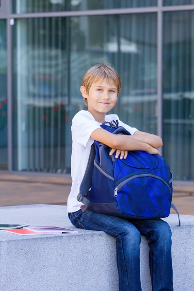 Garçon assis avec son sac à dos, livres et tablette ordinateur en plein air . — Photo