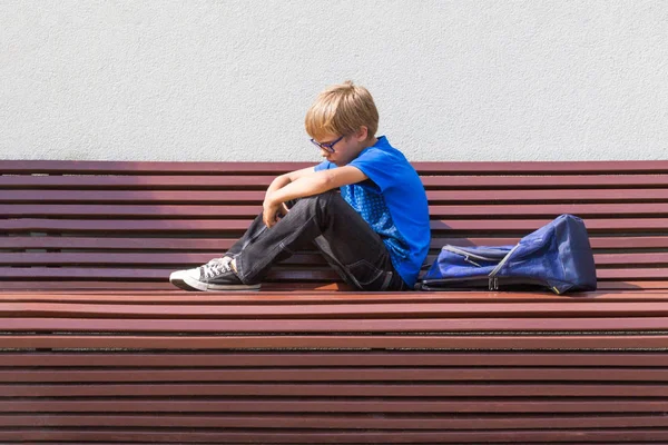 Niño triste y cansado sentado solo en el banco al aire libre . — Foto de Stock