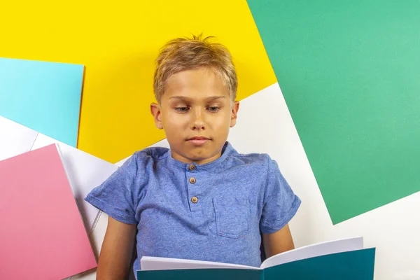 小学生男孩读书笔记本做作业。顶部视图, 彩色背景 — 图库照片