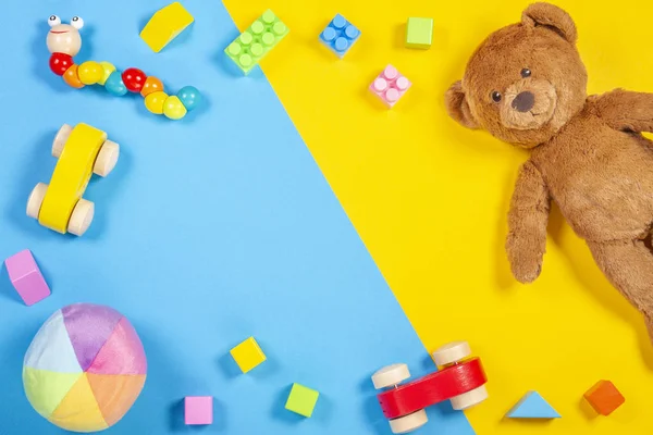Crianças bebê brinquedos quadro com ursinho de pelúcia, carro de brinquedo de madeira, tijolos coloridos no fundo azul e amarelo. Vista superior — Fotografia de Stock