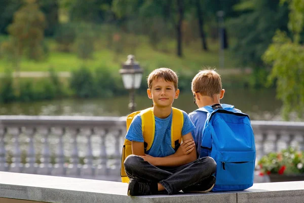 Educación primaria, vuelta a la escuela, amistad, infancia, comunicación y gente cóncava - niños con mochila sentados al aire libre — Foto de Stock