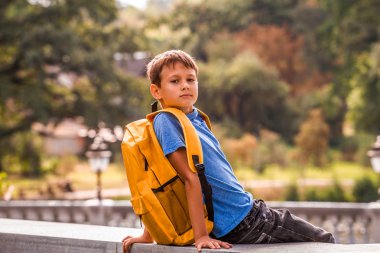 Okuldan sonra açık havada oturup sırt çantası ile sevimli akıllı çocuk.