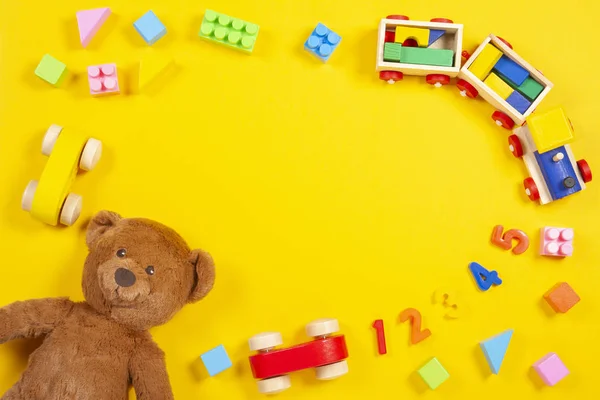 Bambino bambini giocattoli sfondo con orsacchiotto, treno di legno, blocchi colorati e mattoni su sfondo giallo. Vista dall'alto — Foto Stock